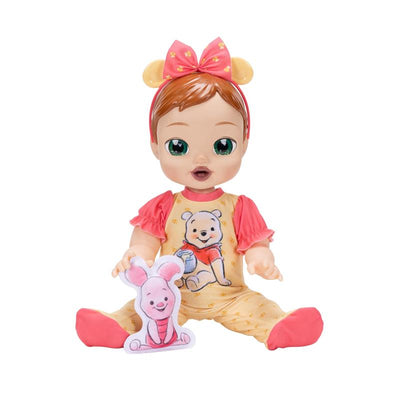Interactive baby doll dressed in Pooh-themed outfit with a matching bow, holding a small stuffed Piglet toy.