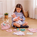 A girl sitting on the floor holds a 15.5” Bonbebé weighted reborn baby doll among various play accessories.
