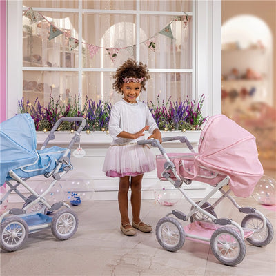 A young girl in a white top and pink tutu stands beside two toy strollers, one pink and one blue, in a bright room.