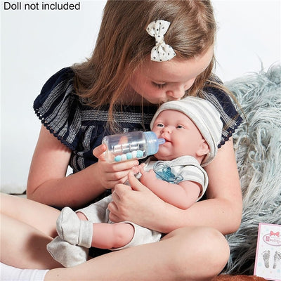 A young girl holds a baby doll, feeding it with a blue baby bottle, while wearing a navy striped blouse and polka-dot bow.