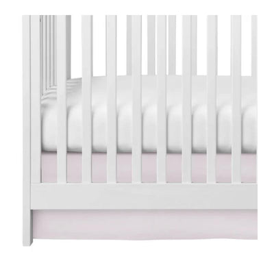 Pink crib skirt for baby bed, displayed under a white crib with a white mattress.