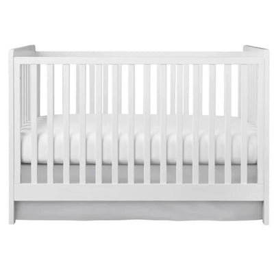 Gray crib skirt for baby bed, complementing a white crib with a padded white mattress visible inside.