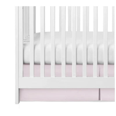 Pleated pink crib skirt positioned under a white crib, enhancing the nursery decor.