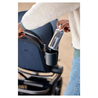Hand placing a clear water bottle into a black cup holder attached to a stroller, showcasing the Joolz Cup Holder.