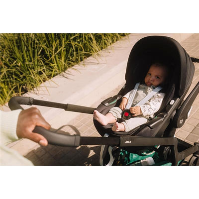 Car seat adapter set for Joolz Hub2 stroller with a baby seated in the car seat, securely fastened, on a sidewalk.
