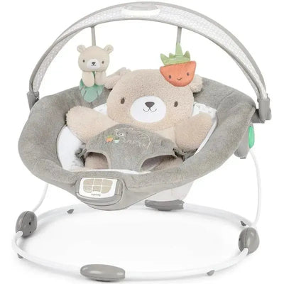 Ingenuity InLighten Baby Bouncer Seat in Natem color with a plush bear toy and hanging animal plushies.