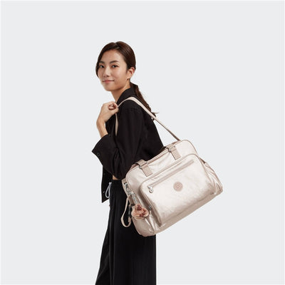 Kipling Alanna Baby Bag in Quartz Metallic being carried by a woman, featuring a zippered front pocket and floral keychain.