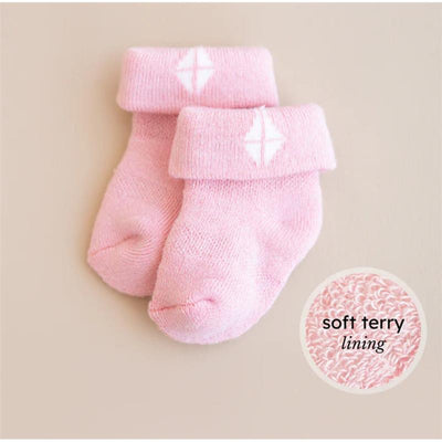 Pastel pink baby socks with a cuff and a white diamond logo, featuring a soft terry lining.