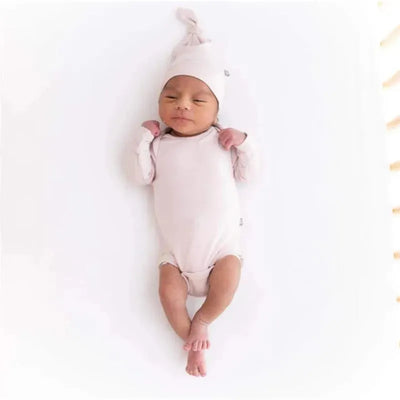 Bamboo baby knotted cap in blush color on a sleeping infant, dressed in a matching soft onesie, posed on a white background.