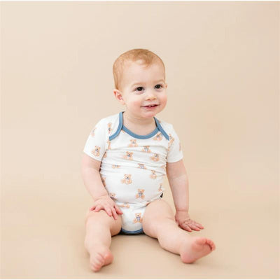 Smiling baby wearing a Kyte Baby bodysuit featuring teddy bear prints, seated against a neutral background.