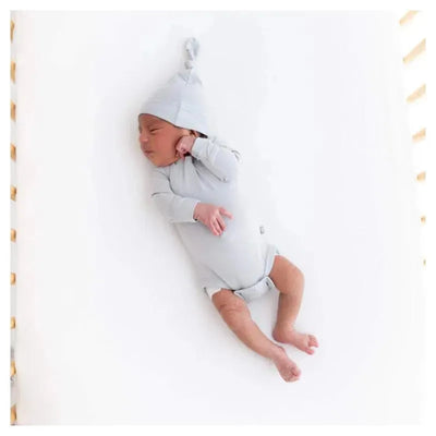 Newborn baby sleeping on a white surface, wearing a light gray long sleeve bodysuit and a matching hat.