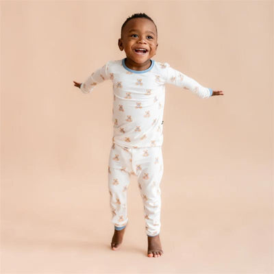 Child wearing Kyte Baby long sleeve pajamas featuring a teddy bear print, smiling with arms outstretched against a neutral background.