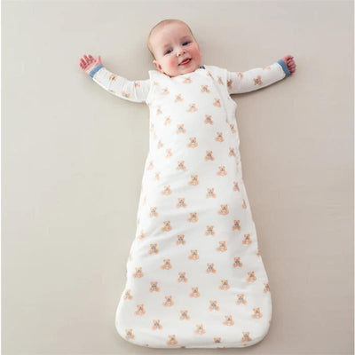 Infant wearing a Kyte Baby sleep bag, featuring teddy bear prints, lying on a neutral surface with arms outstretched.