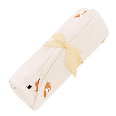 Kyte Baby swaddle blanket in fluffy dog design, rolled and tied with a yellow ribbon, featuring playful dog illustrations.