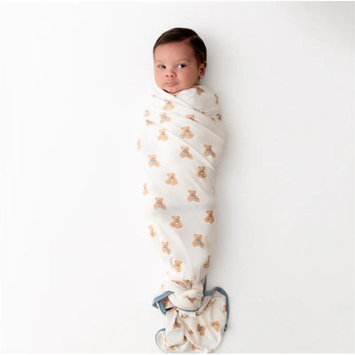 Infant swaddled in a Kyte Baby blanket featuring teddy bear prints and a blue trim, on a white background.