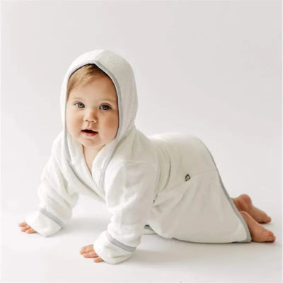 Toddler wearing a white bath robe with a hood and storm trim, crawling on a light background.