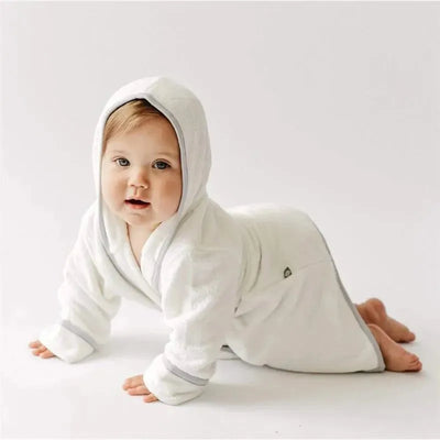Toddler wearing a white bathrobe with a hood and gray trim, crawling on a light background.