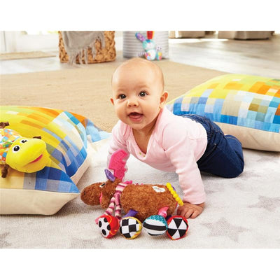 Baby playing on the floor with Lamaze Muffin the Moose toy, surrounded by colorful pillows and fabric patterns.