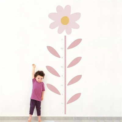 Growth chart wall decal featuring a pink flower and measurement scale. A child stands beside it, reaching up.