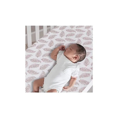 Baby sleeping on a lambs and ivy leaves patterned fitted crib sheet in a white crib.