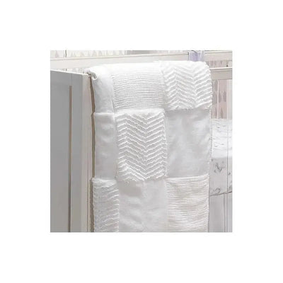 White patchwork quilt with textured patterns, draped over the edge of a crib, showcasing a soft, neutral design.