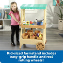 Kid-sized farmstand featuring an easy-grip handle, rolling wheels, and colorful toy fruits and vegetables in baskets.