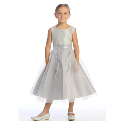 Silver baby girl dress with shimmer tulle overlay and sequined waistband, worn by a smiling young girl.