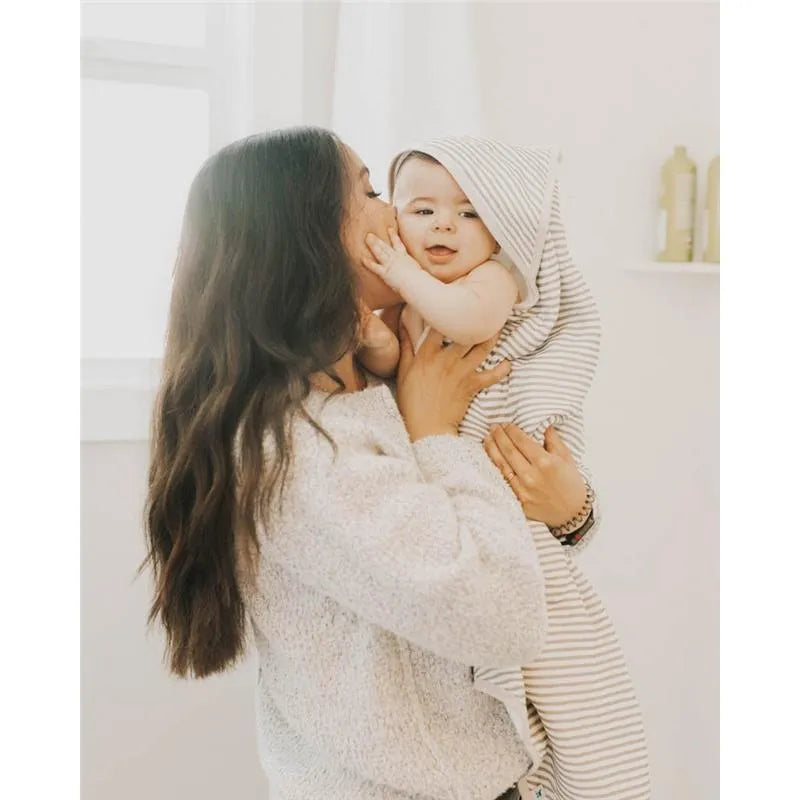 A woman lovingly holds a smiling baby wrapped in a grey-striped hooded towel, showcasing a cozy setting.