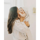 A woman lovingly holds a smiling baby wrapped in a grey-striped hooded towel, showcasing a cozy setting.
