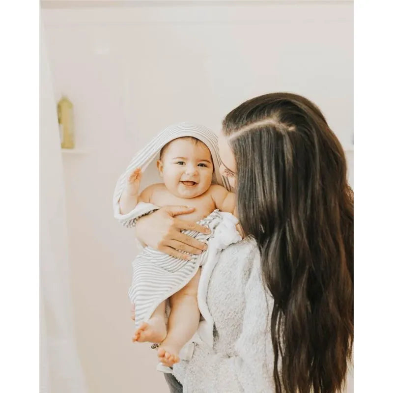 Hooded towel with grey stripes on a baby, being held and smiled at by an adult in a soft setting.