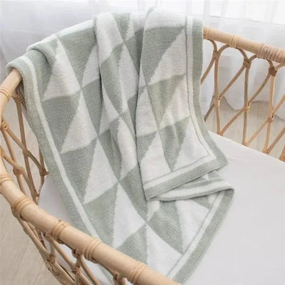 Chenille baby blanket in sage, featuring a soft, thick texture and a triangle pattern, draped over a crib.
