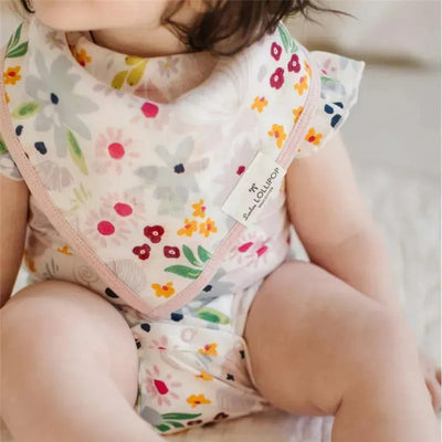 Loulou Lollipop muslin bib set in shell floral pattern worn by a baby, featuring colorful floral designs and the brand label.
