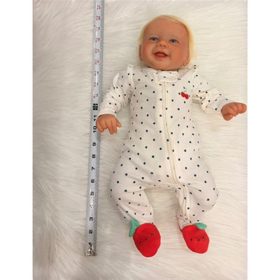 Reborn baby doll Viviene made of white vinyl, wearing a polka dot onesie and red strawberry booties, measuring with ruler beside it.