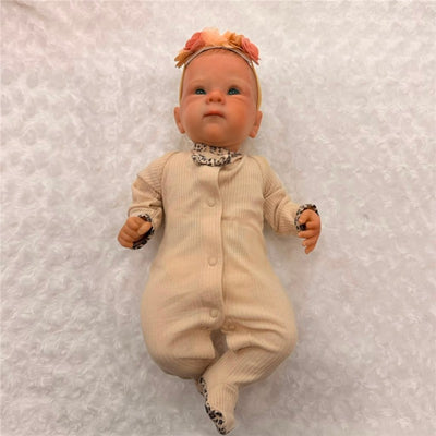 Reborn baby doll in a beige outfit with leopard print accents, featuring open green eyes and painted hair.