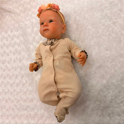 Reborn baby doll with painted hair, open green eyes, wearing a beige outfit with a floral headband.