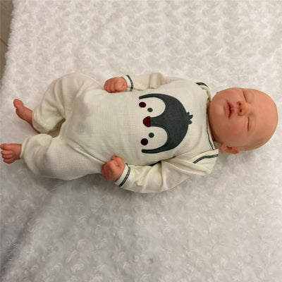 Vinyl reborn baby doll named Jackson, with painted hair, wearing a penguin-themed outfit, lying on a soft blanket.