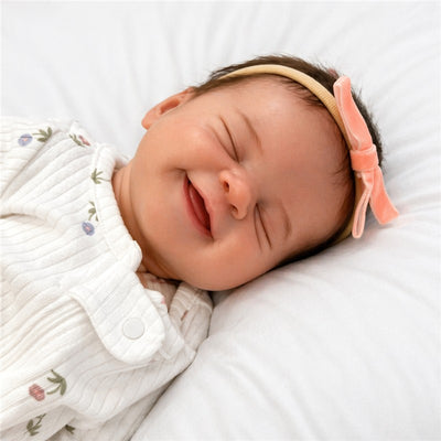 Reborn Baby Doll with smiling expression, wearing a white outfit and pink headband, resting on a soft surface.
