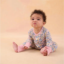 Baby sitting in a floral-patterned Modal magnetic coverall with pink accents, making a playful expression.