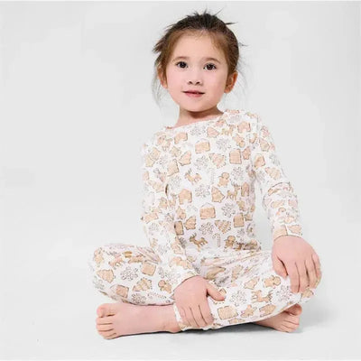 Organic cotton long sleeve set featuring a child seated, wearing a patterned outfit with gingerbread and holiday-themed prints.