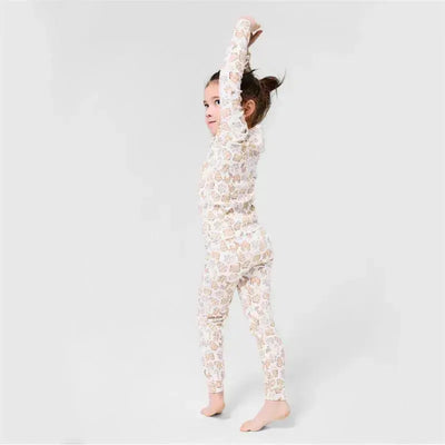 Child in a long sleeve organic cotton set featuring a gingerbread pattern, stretching with a playful expression.