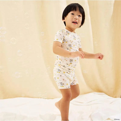 Child in short-sleeve pajama set featuring Mickey Mouse, playing on a soft surface with a light background.