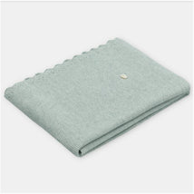 Sweater knit cotton blend blanket in Pravia sage color, featuring a scalloped edge and a small decorative tag.