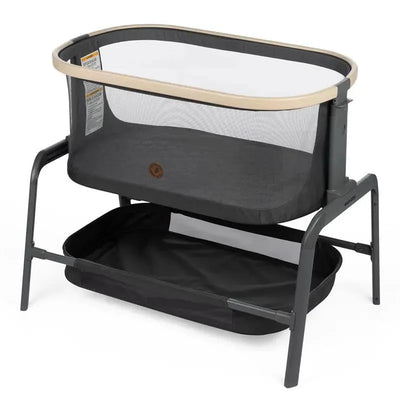 Maxi-Cosi Iora Bedside Bassinet in Classic Graphite, featuring a mesh side, wooden accents, and a storage shelf below.