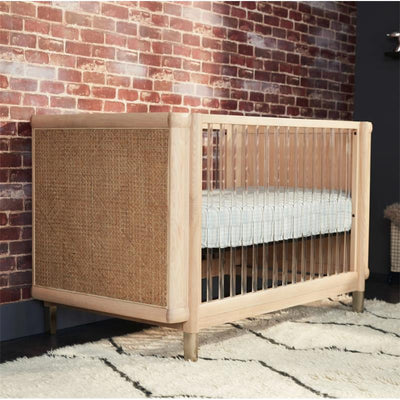 4-in-1 convertible crib with a wooden frame and woven side panel, featuring a fitted mattress on a patterned base.