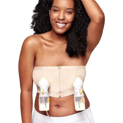 Hands-free pumping bustier by Medela in chai color, worn by a smiling woman, holding breast pump attachments.