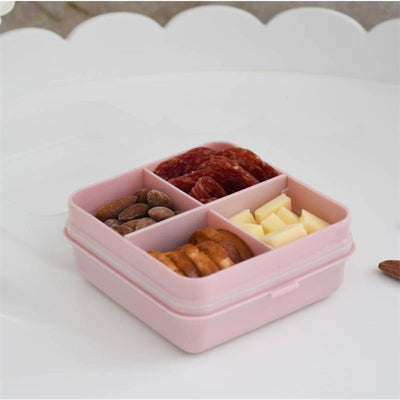 Petite pink Snackle Box with four compartments, filled with nuts, cheese, salami, and crackers.