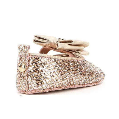 Rose gold ballet crib shoe by Michael Kors with a sparkly finish and a decorative bow on top.