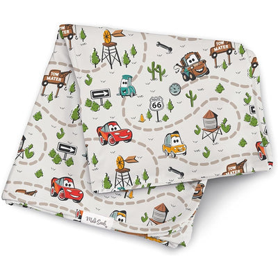 Milk Snob Cars swaddle blanket featuring colorful illustrations of cars, roads, and landmarks on a light background.