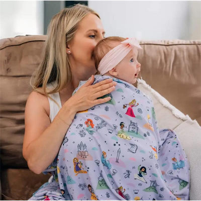 Swaddled in a colorful Disney Princess-themed blanket, a mother gently hugs her surprised baby on a couch.
