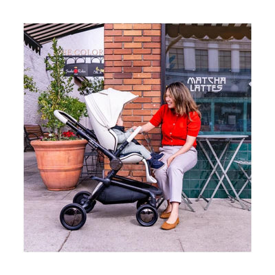 Mima Creo Single Stroller in white, with a woman engaging with a child seated inside, outdoors by a café.